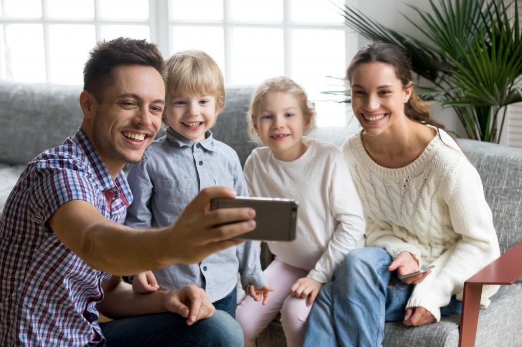 Happy young family with adopted kids smiling taking selfie toget